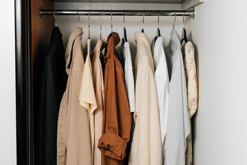 Beige, brown and white t-shirts and shirts hang on hangers in the closet. The concept of a summer wardrobe