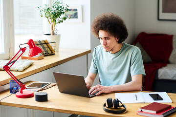 Young man sitting at table and typing on laptop, he working online at home