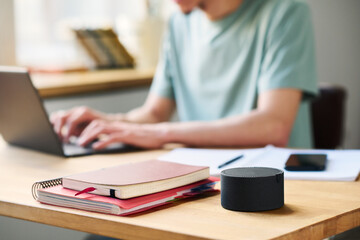 Close-up of smart speaker standing on table with books with man working online on laptop in background