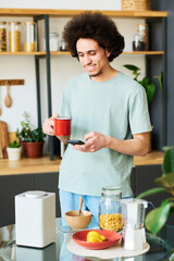 Fototapeta na wymiar Vertical image of young man connecting smartphone with smart speaker to listen to music during his breakfast in the kitchen