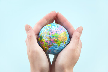 Women's hands hold a globe in their hands on a light blue background.