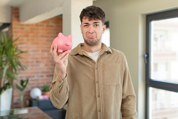 young handsome man feeling sad and whiney with an unhappy look and crying. piggy bank concept