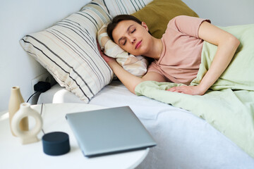 Young woman resting on bed in her bedroom after using gadgets