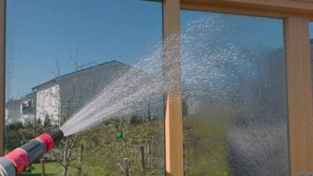 Close uo view of wetting facade windows with water using garden hose before washing them. Slow motion. Sweden.
