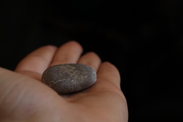 Fototapeta na wymiar hand holding a grey river stone in black background