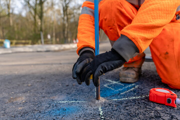 Fototapeta na wymiar Builder marking future finish road levels on a road setting out steel pins with yellow electric tape on a road improvement project