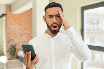 young  adult man looking happy, astonished and surprised. smartphone concept