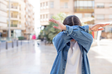 pretty young adult woman covering face with hand and putting other hand up front to stop camera,...