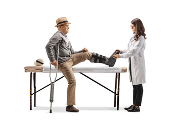 Elderly man with a leg brace sitting on a bed and a female doctor checking his foot