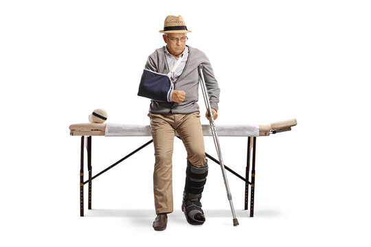 Senior man with a broken arm and leg sitting on a bed for physical therapy