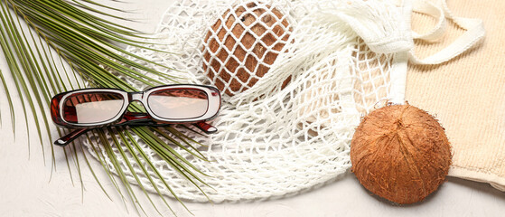 Sunglasses with palm leaf, string bag, towel and coconuts on light background