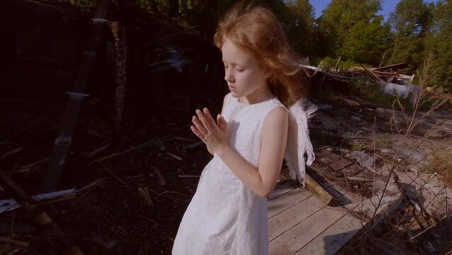 Sad child girl on the background of a burned-out house. Child angel near the destroyed house.