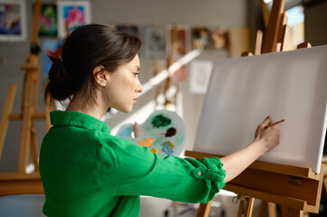 Young woman starting to draw on blank empty canvas with oil paints in art studio