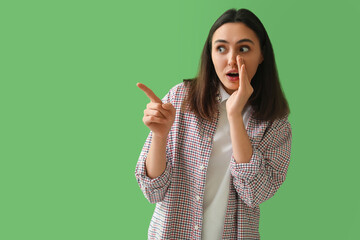 Fototapeta premium Shocked young woman pointing at something on green background