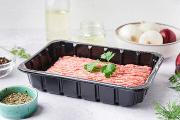 Plastic package with fresh minced meat, parsley and spices on white grunge background
