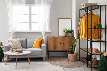 Interior of living room with shelving unit, clothes and sofa