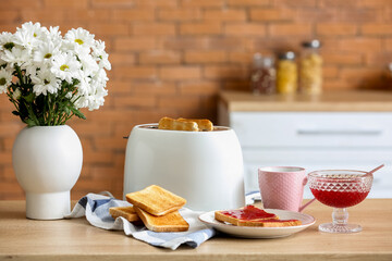 Modern toaster with crispy bread slices and sweet jam toasts on table in kitchen