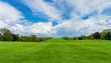 Wide grass filled view lined with trees in English parkland with dramatic sky