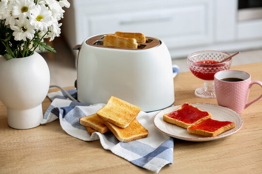 Modern toaster with crispy bread slices and sweet jam toasts on table in kitchen