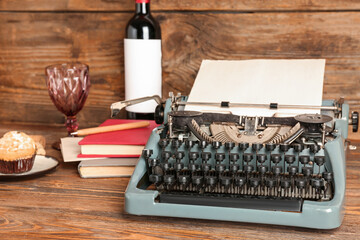 Vintage typewriter, bottle of wine, glass, muffin and books on wooden table