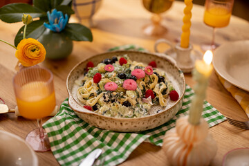 Tasty pasta with spinach and berries decorated with edible flowers on a plate for sharing at beautifuly served dining table