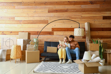 Happy young couple with book sitting in room on moving day