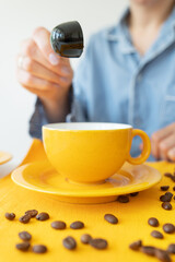 A young woman prepares herself coffee in a bright yellow mug. Grains of coffee on the table. Enjoy fresh aromatic coffee.