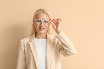Mature blonde woman in eyeglasses on beige background