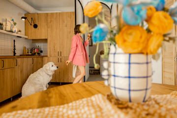 Fototapeta na wymiar Woman in pink suit spends leisure time with her dog in modern and stylish apartment. Domestic lifestyle