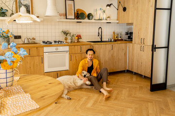 Man spends leisure time happily with a dog at kitchen of his stylish apartment. Friendship with pets and domestic lifestyle concept