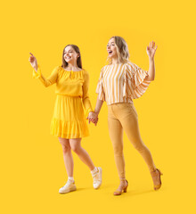 Young sisters holding hands on yellow background