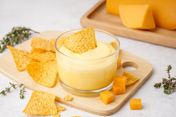 Board with bowl of tasty cheddar cheese sauce and nachos on white grunge background