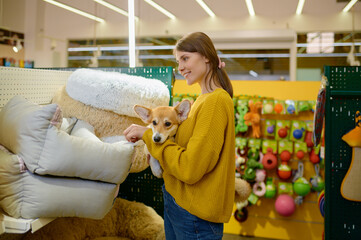 Young woman holding corgi dog on hands choosing sleeping place at pet shop