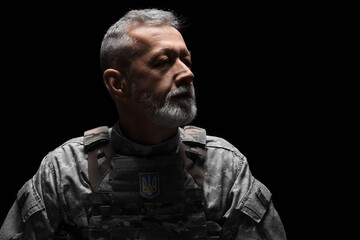Obraz premium Mature soldier with Ukrainian coat of arms patch on dark background, closeup