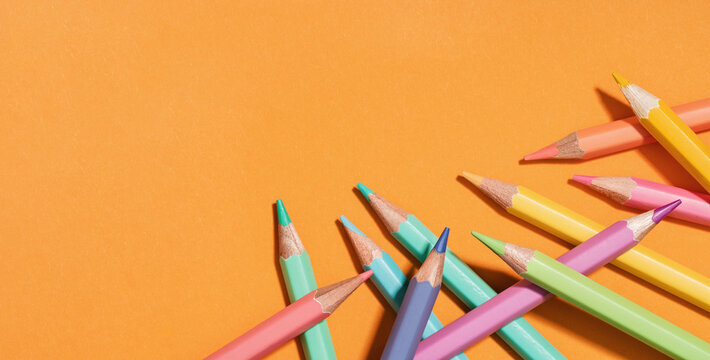 Colored pastel pencils corner border on orange banner. Back to School or drawing and creativity concept. Copy space. Top view