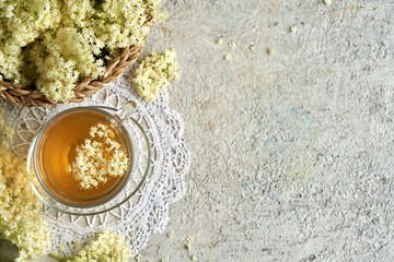 Black elder flowers with a cup of tea on bright background with copy space