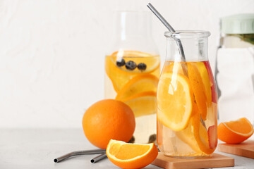 Bottles of infused water with orange slices on white table