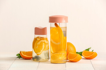 Sports bottles of infused water with orange slices on white tile table
