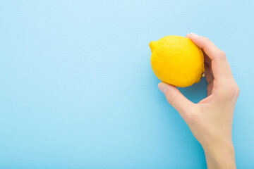 Young adult woman hand holding yellow lemon on light blue table background. Pastel color. Fresh fruit. Closeup. Empty place for text. Top down view.