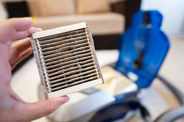 A man removes dust from a  vacuum cleaner air filter, close-up