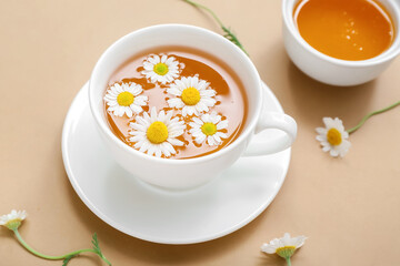 Cup of hot chamomile tea with honey on beige background