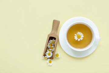 Cup of hot chamomile tea with scoop on pale yellow background
