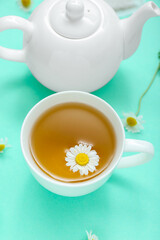 Teapot and cup of hot chamomile tea on turquoise background