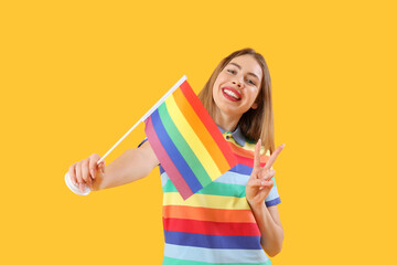 Young woman with LGBT flag showing victory gesture on yellow background