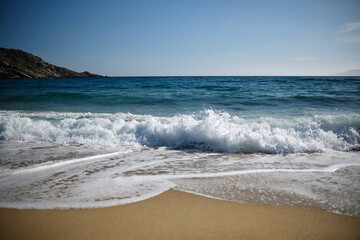Fototapeta na wymiar Waves and sea foam at the windy beach of Mylopotas in Ios Greece