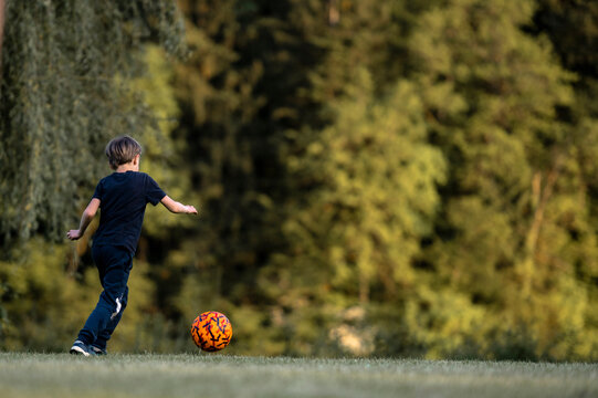 Young boy kickin a ball outside in green meadow