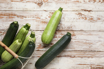 Basket with fresh green zucchini on white wooden background