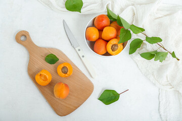 Board and bowl with fresh apricots on white background