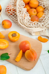 Board and string bag with fresh apricots on white tile table