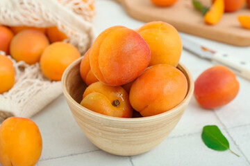 Bowl and string bag with fresh apricots on white tile table